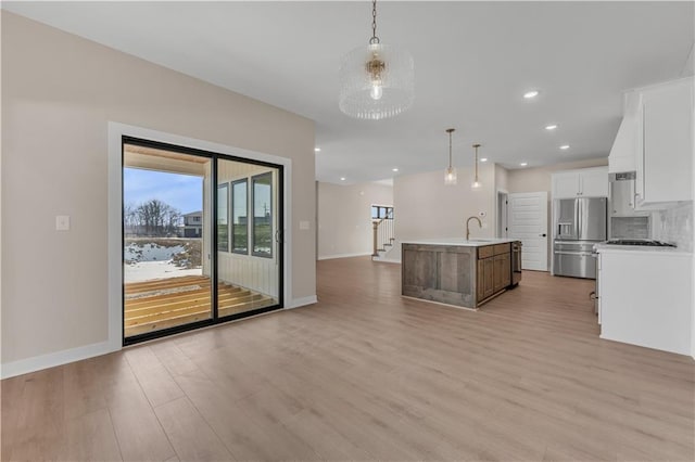 kitchen with light countertops, light wood-style flooring, backsplash, a kitchen island with sink, and stainless steel fridge