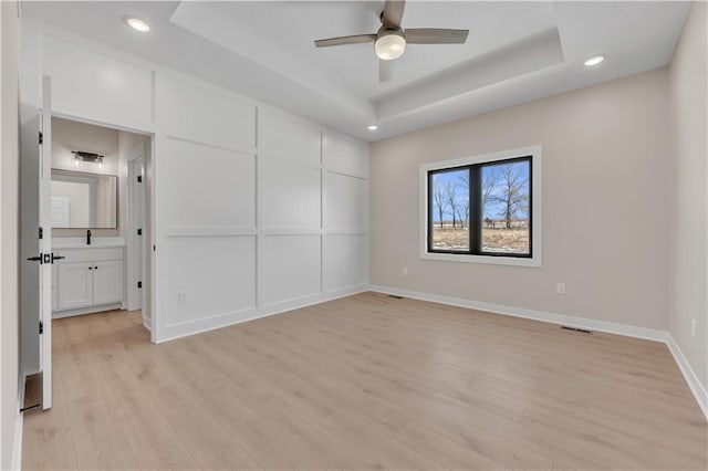 unfurnished bedroom featuring visible vents, baseboards, a tray ceiling, light wood-type flooring, and recessed lighting