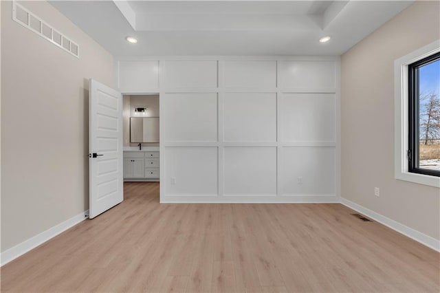 unfurnished bedroom with a tray ceiling, light wood finished floors, visible vents, and baseboards