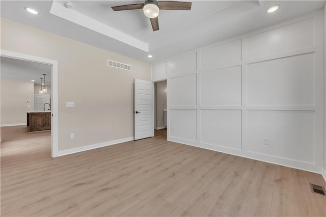 unfurnished bedroom featuring light wood-type flooring, visible vents, and a tray ceiling