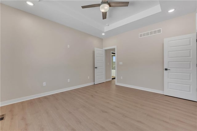 empty room featuring recessed lighting, visible vents, baseboards, a tray ceiling, and light wood finished floors