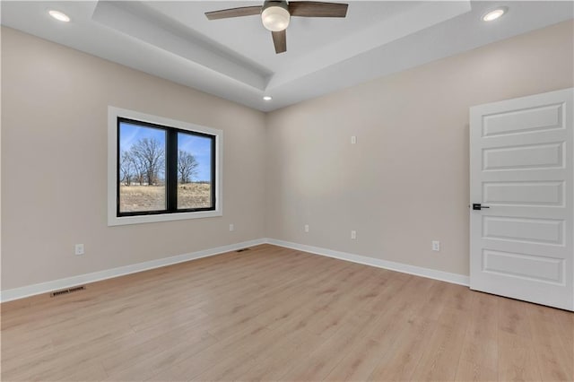 spare room with visible vents, baseboards, a tray ceiling, light wood-style floors, and recessed lighting