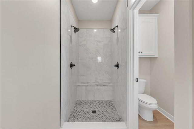 full bathroom featuring wood finished floors, a tile shower, toilet, and baseboards