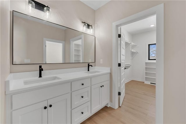 bathroom featuring double vanity, a spacious closet, wood finished floors, and a sink