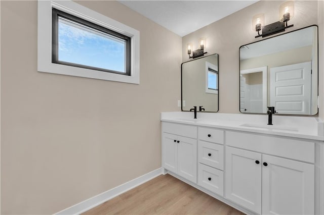 bathroom with double vanity, baseboards, a sink, and wood finished floors