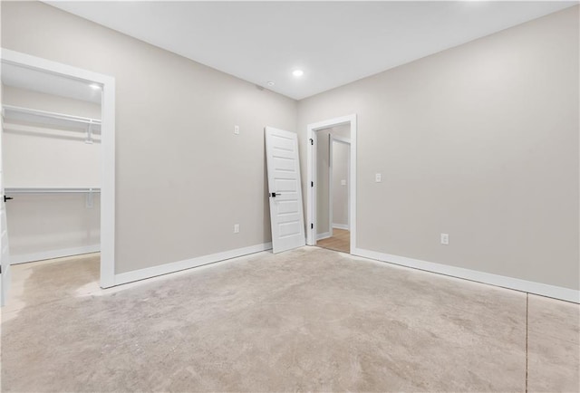 unfurnished bedroom featuring baseboards, a walk in closet, concrete floors, a closet, and recessed lighting