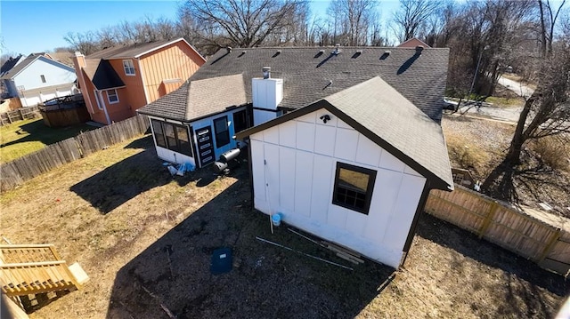 exterior space featuring roof with shingles, a chimney, board and batten siding, a sunroom, and a fenced backyard