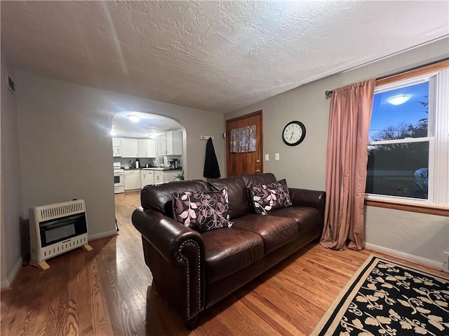 living room with arched walkways, a textured ceiling, heating unit, and wood finished floors