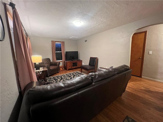 living room featuring a textured ceiling, wood finished floors, arched walkways, baseboards, and a textured wall