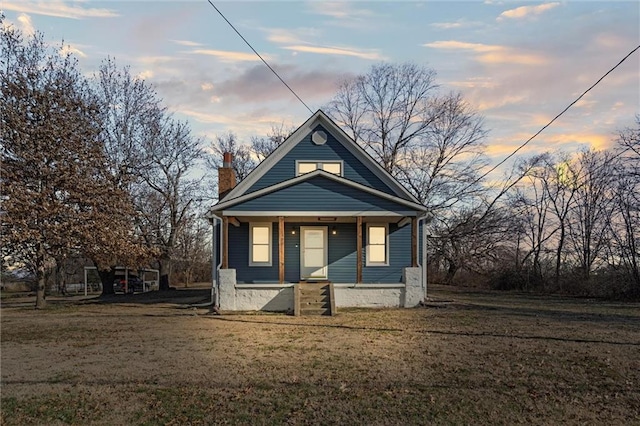 view of front of house featuring a yard, covered porch, and a chimney