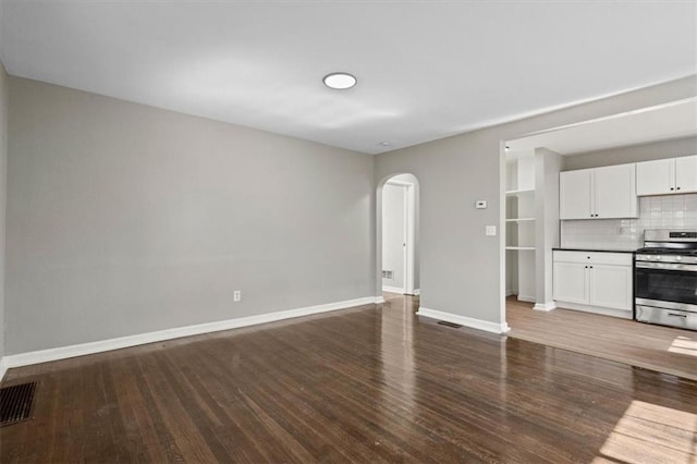 unfurnished living room with baseboards, visible vents, arched walkways, and wood finished floors