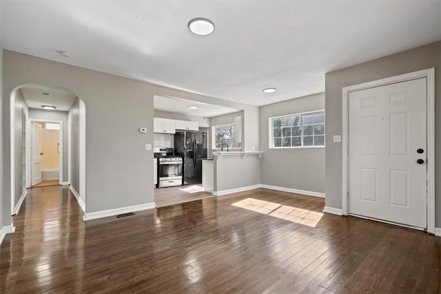 unfurnished living room featuring dark wood-style floors, baseboards, visible vents, and arched walkways