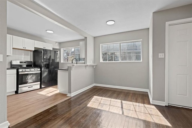 kitchen with stainless steel gas range oven, a peninsula, white cabinets, backsplash, and black refrigerator with ice dispenser