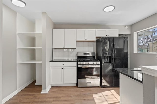 kitchen with tasteful backsplash, stainless steel gas range oven, white cabinets, light wood-style floors, and black fridge