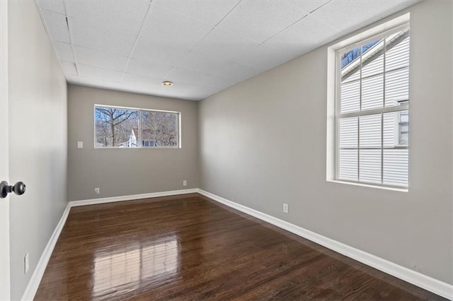 empty room featuring dark wood-style floors, a drop ceiling, and baseboards