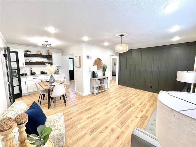 living area featuring light wood finished floors, visible vents, baseboards, a textured ceiling, and crown molding