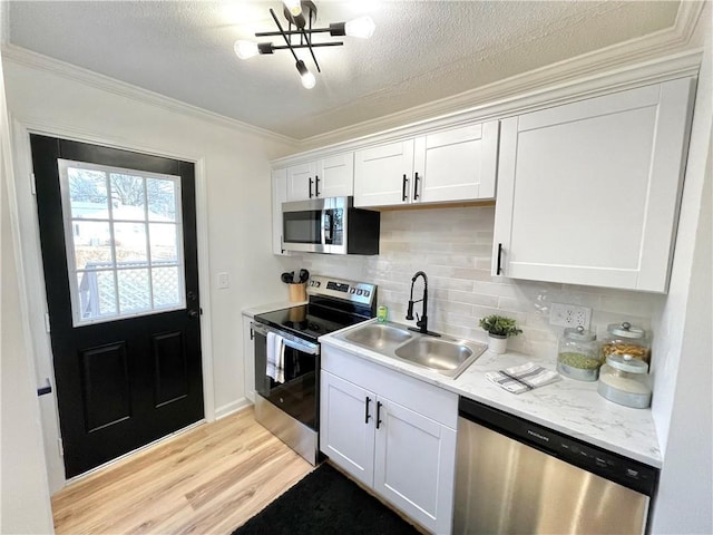 kitchen with light wood finished floors, decorative backsplash, appliances with stainless steel finishes, ornamental molding, and a sink