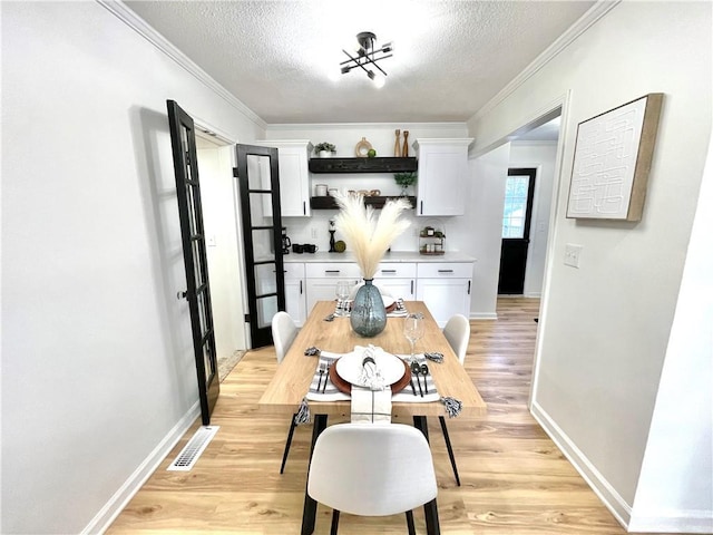 dining room featuring light wood finished floors, crown molding, visible vents, and a textured ceiling