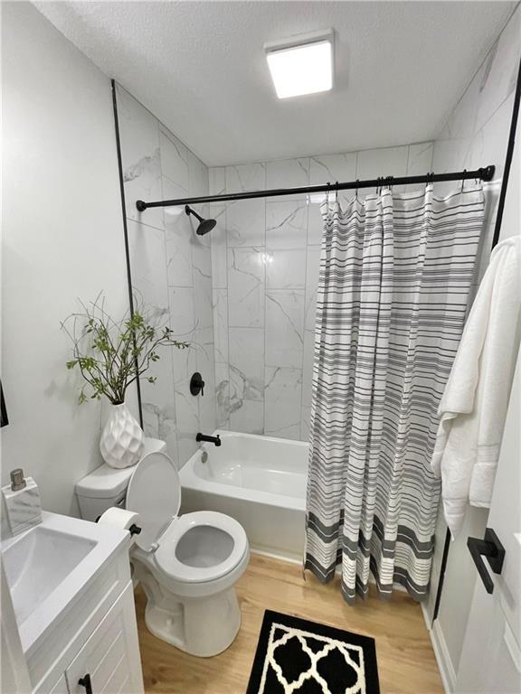 bathroom with shower / tub combo, toilet, wood finished floors, a textured ceiling, and vanity