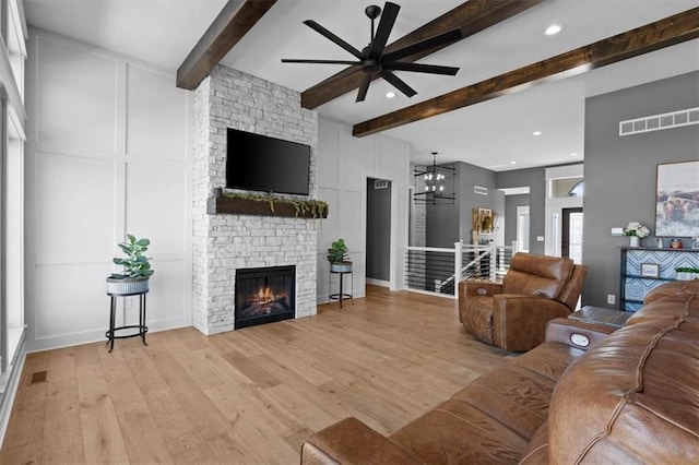 living room with visible vents, beamed ceiling, light wood-style floors, a fireplace, and a decorative wall