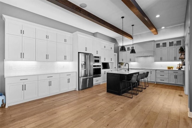 kitchen with light wood-style flooring, appliances with stainless steel finishes, a kitchen breakfast bar, a kitchen island with sink, and light countertops