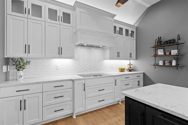 kitchen with black electric cooktop, white cabinets, vaulted ceiling, light wood-type flooring, and light stone countertops