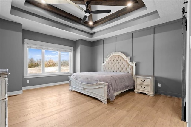 bedroom with ceiling fan, a tray ceiling, light wood-style flooring, and baseboards