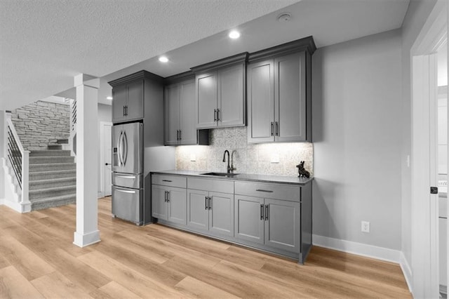 kitchen with light wood-style flooring, a sink, gray cabinetry, stainless steel refrigerator with ice dispenser, and backsplash