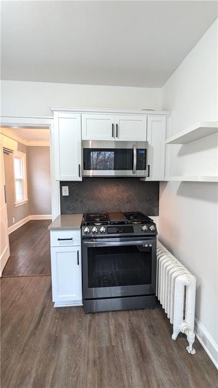 kitchen featuring radiator heating unit, appliances with stainless steel finishes, dark wood-style flooring, white cabinetry, and backsplash