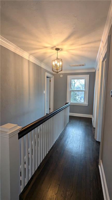 corridor featuring ornamental molding, a notable chandelier, baseboards, and dark wood-style floors