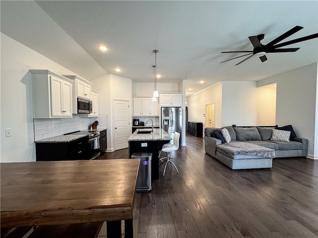 kitchen featuring a breakfast bar area, a sink, open floor plan, appliances with stainless steel finishes, and light stone countertops