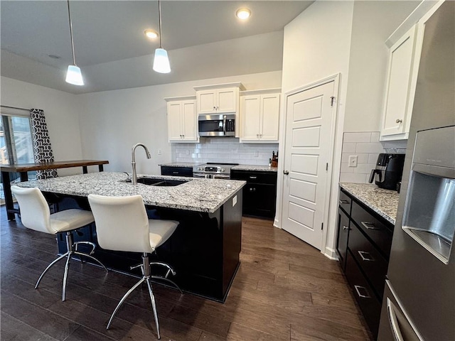 kitchen featuring stainless steel appliances, a breakfast bar, dark wood-style flooring, a sink, and white cabinetry