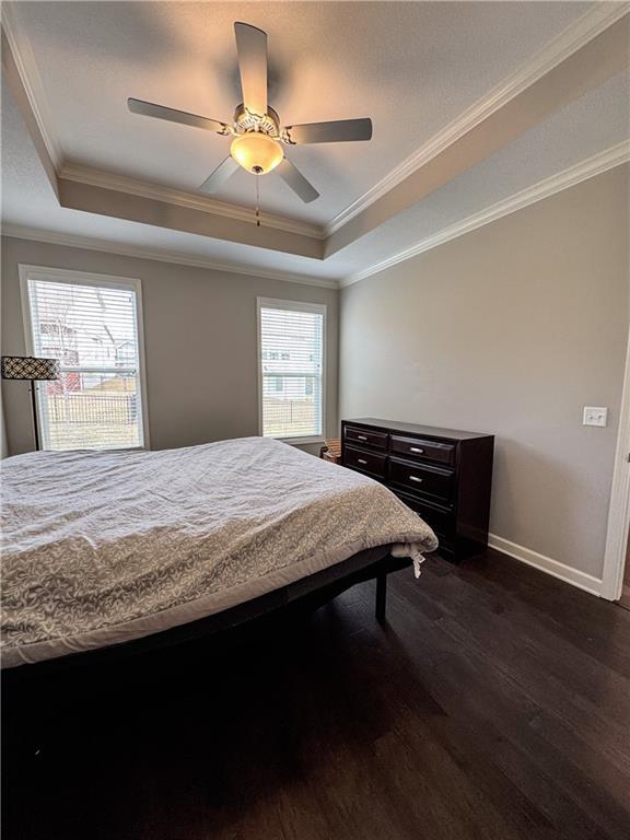 bedroom featuring dark wood-style floors, a tray ceiling, ornamental molding, and baseboards