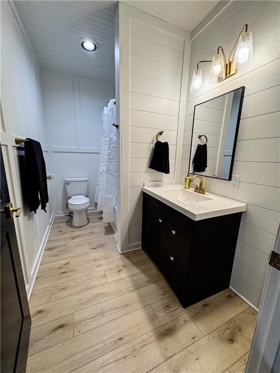 bathroom with curtained shower, a decorative wall, toilet, vanity, and wood finished floors