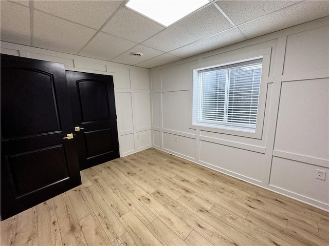 spare room featuring light wood-style floors, visible vents, a decorative wall, and a drop ceiling