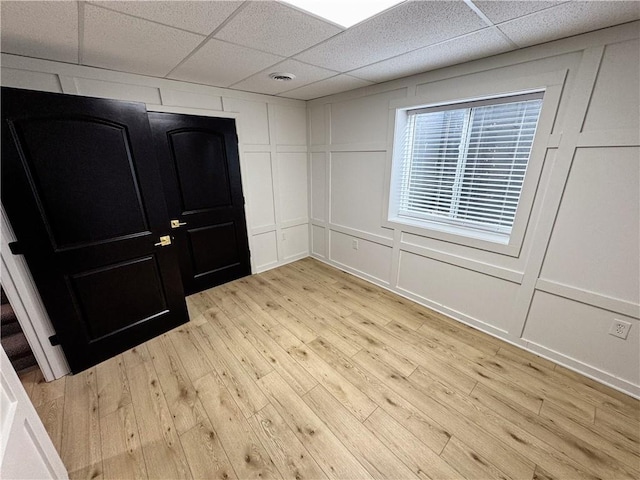 empty room with light wood-style floors, visible vents, a decorative wall, and a drop ceiling