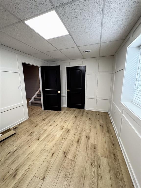 spare room with stairs, light wood-type flooring, visible vents, and a decorative wall