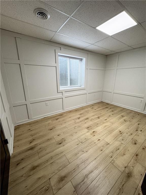 spare room featuring light wood-type flooring, visible vents, and a decorative wall