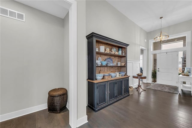 entrance foyer with dark wood-style floors, baseboards, visible vents, and a notable chandelier