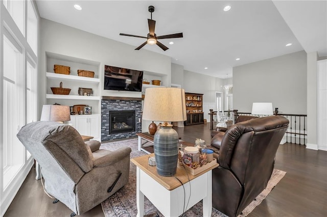 living room with ceiling fan, recessed lighting, dark wood-type flooring, built in features, and a tiled fireplace