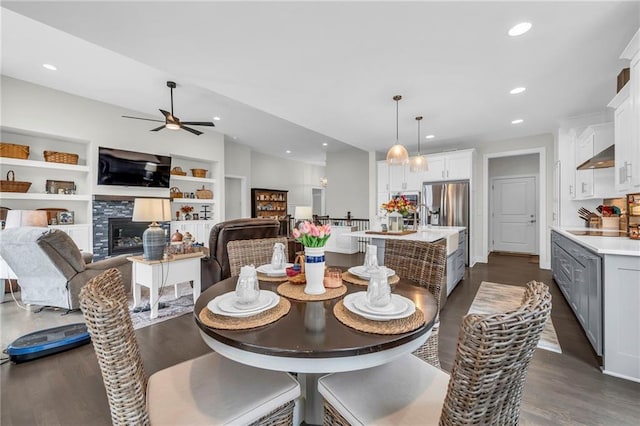 dining room featuring built in features, a ceiling fan, a tile fireplace, dark wood-style flooring, and recessed lighting