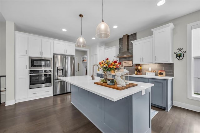 kitchen featuring tasteful backsplash, stainless steel appliances, light countertops, wall chimney range hood, and a sink