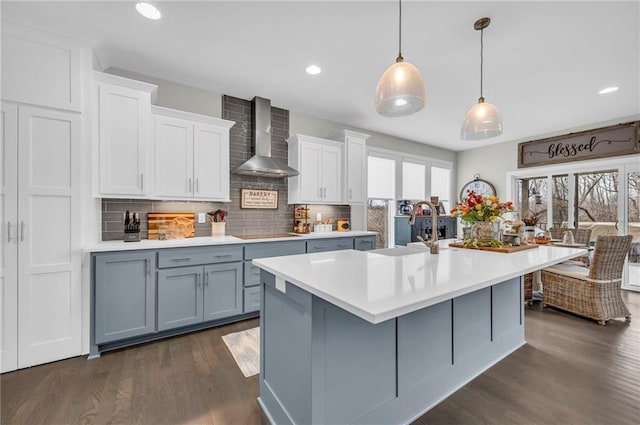 kitchen with wall chimney exhaust hood, light countertops, a sink, and a wealth of natural light