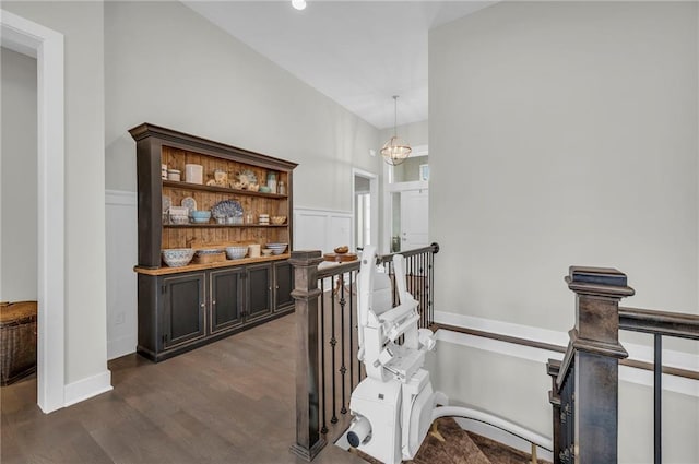 hall with dark wood-style flooring, a wainscoted wall, a decorative wall, and an upstairs landing