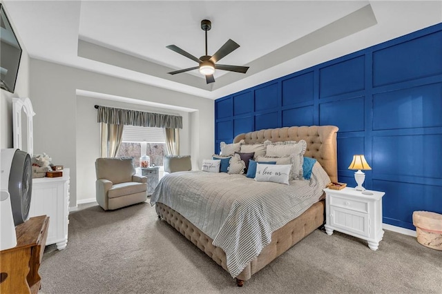 carpeted bedroom with ceiling fan, a tray ceiling, and a decorative wall