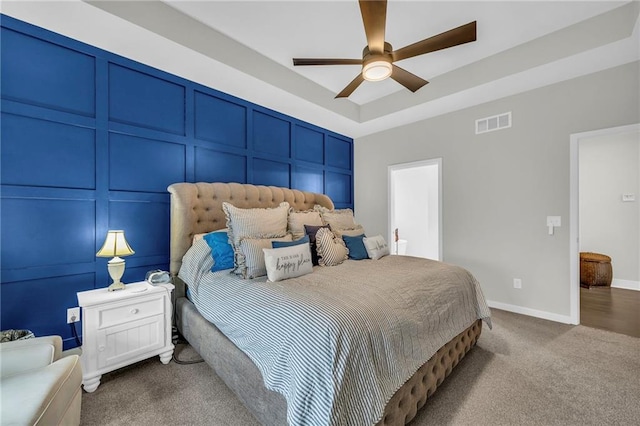 bedroom featuring a decorative wall, visible vents, baseboards, a tray ceiling, and carpet