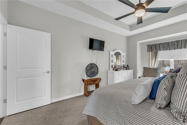 carpeted bedroom featuring a ceiling fan, a tray ceiling, and baseboards