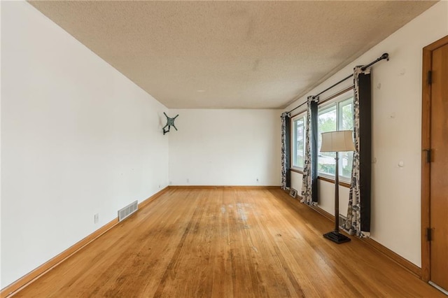 unfurnished room featuring baseboards, visible vents, light wood-style floors, and a textured ceiling