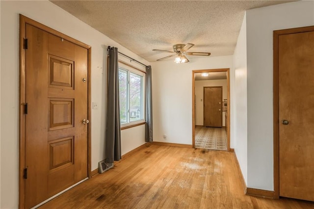 interior space with a textured ceiling, baseboards, ceiling fan, and light wood-style flooring