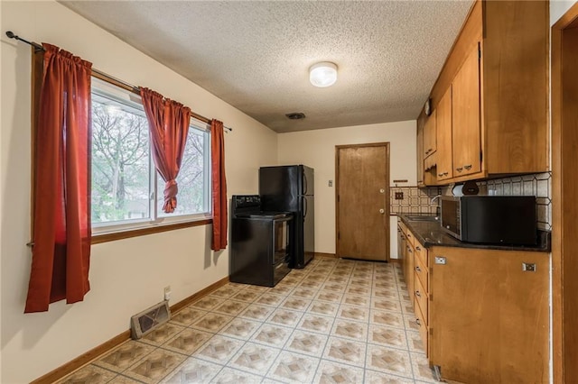 kitchen with tasteful backsplash, dark countertops, visible vents, black appliances, and brown cabinetry